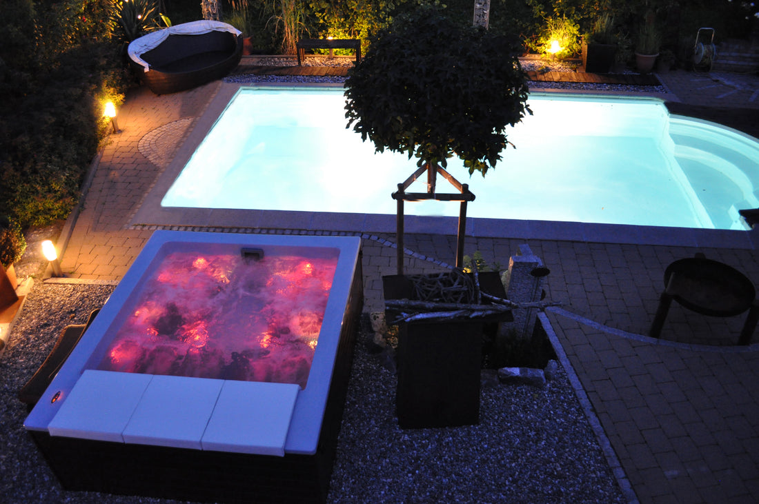 Bañera de hidromasaje y piscina iluminadas por la noche.