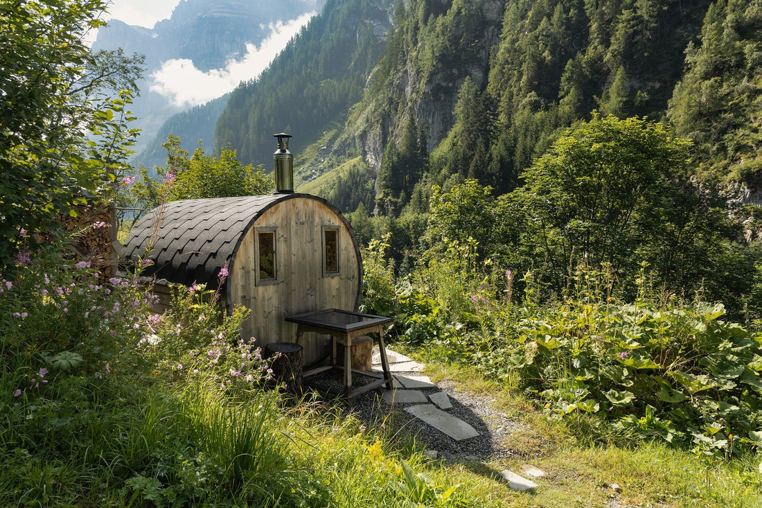 Pequeña sauna de madera en un bosque con mesa al aire libre.