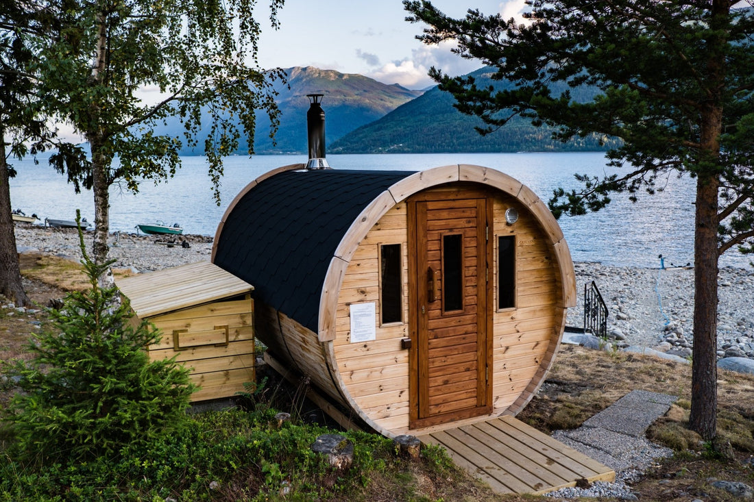 Sauna de barril con techo negro junto a un lago.