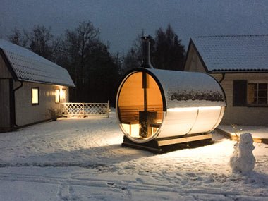 Sauna de barril en un entorno nevado con iluminación interior.