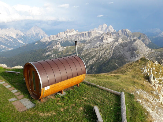 Sauna de barril en una colina con montañas al fondo.