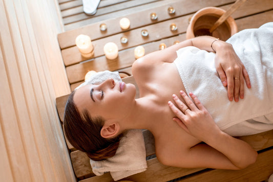 Una mujer se relaja en una sauna con velas, junto a un cubo de agua.