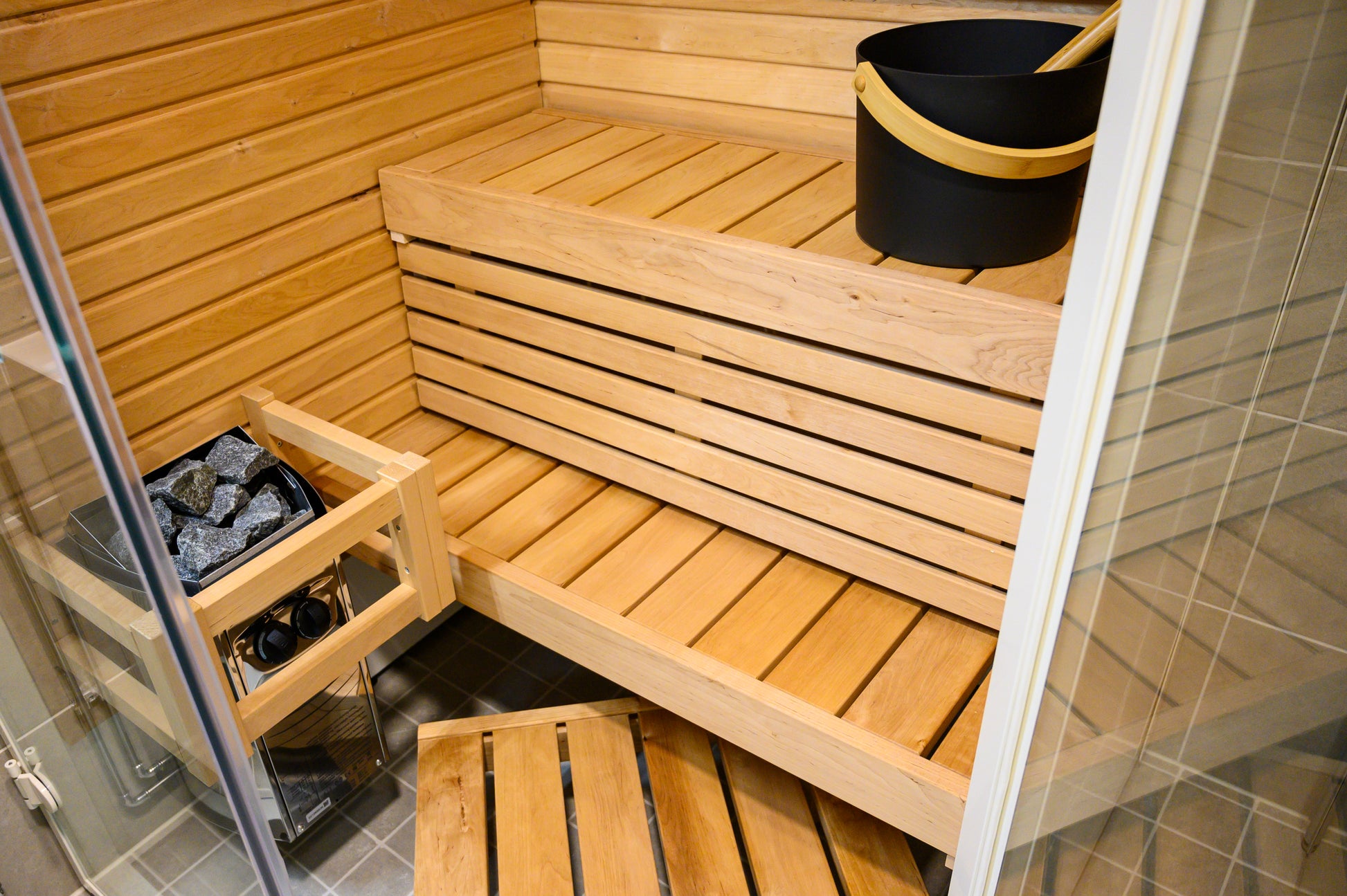 Sauna Sirius Corner con bancos de madera y cubo negro.