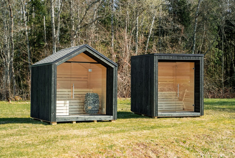 Sauna exterior LUMI aislada con puerta de cristal, en una zona verde.