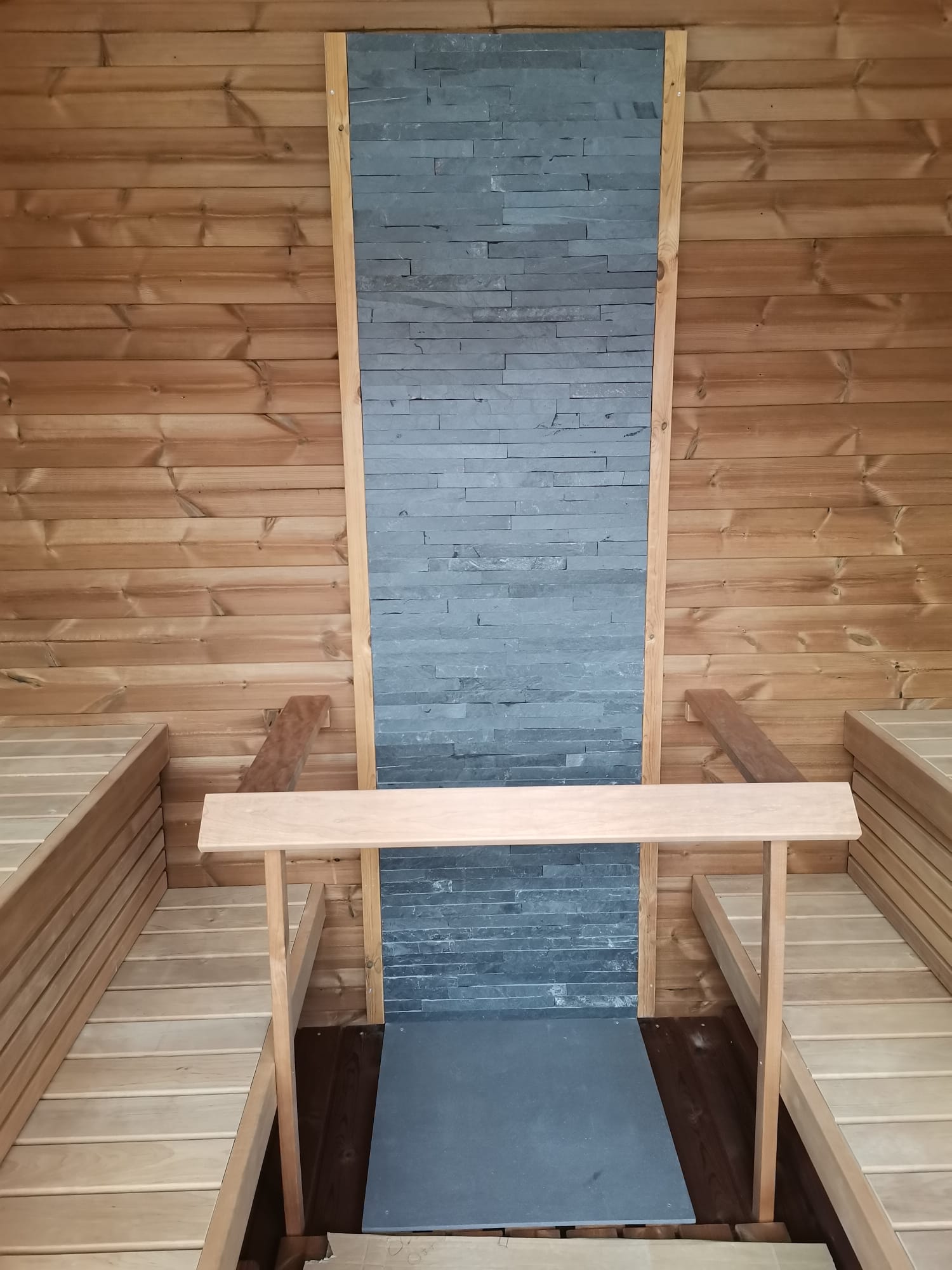 Saunamo Sauna Cubus con pared de piedra y bancos de madera.