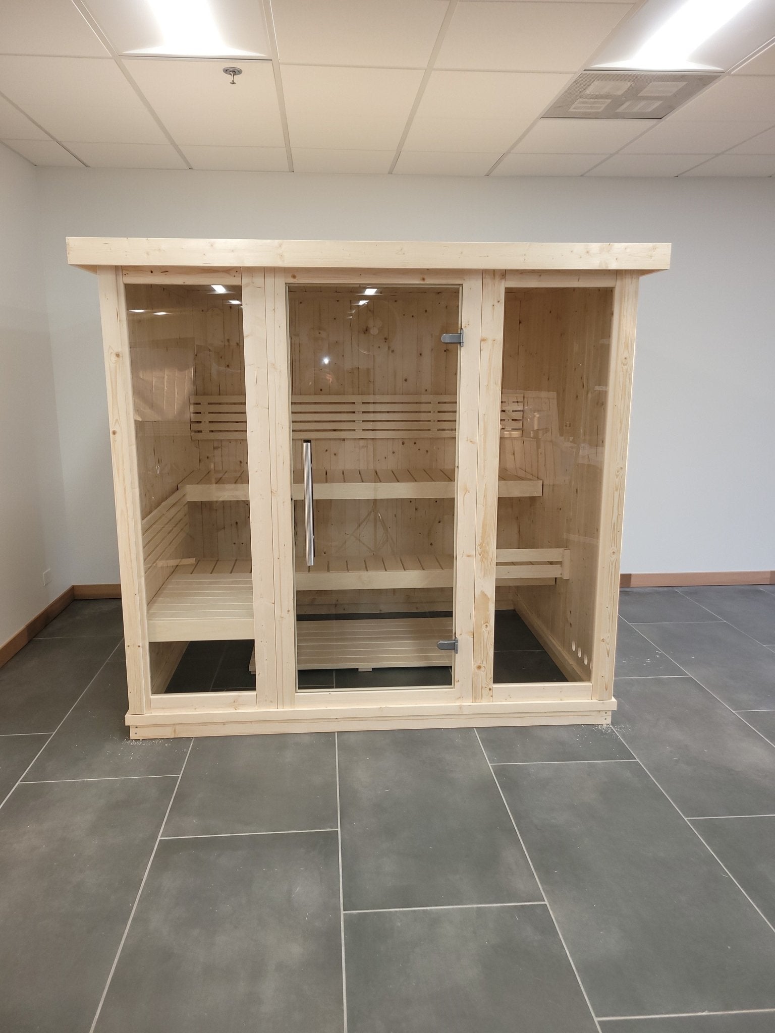 Amplia sauna interior de madera con puertas de cristal templado.